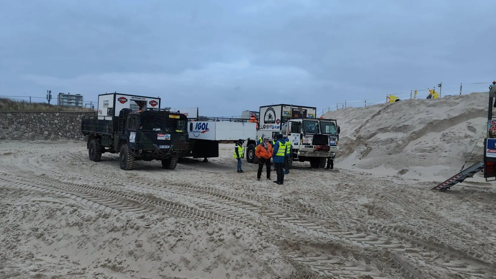Camions d’assistance sur le sable de la plage, personnes en gilet fluorescent au premier plan