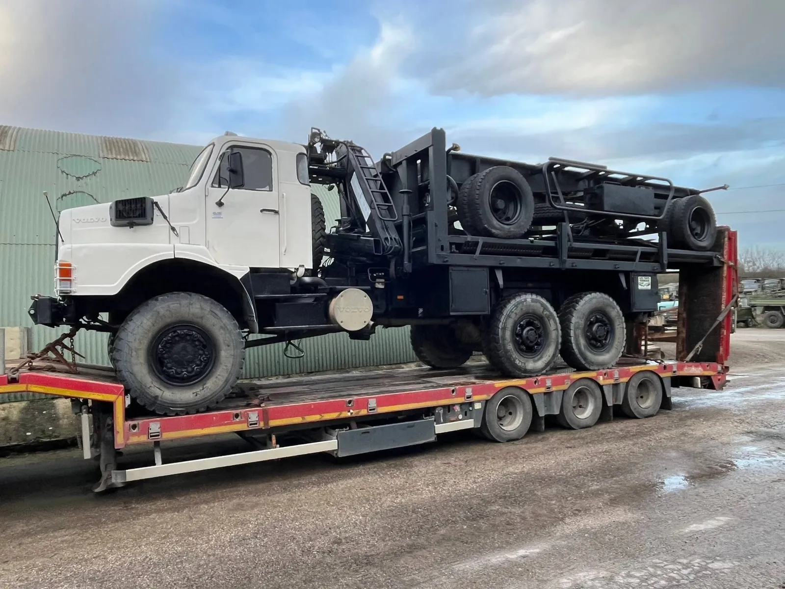 Volvo N10 6x6 blanc à grue portant une remorque retournée, arrimé sur porte-engins