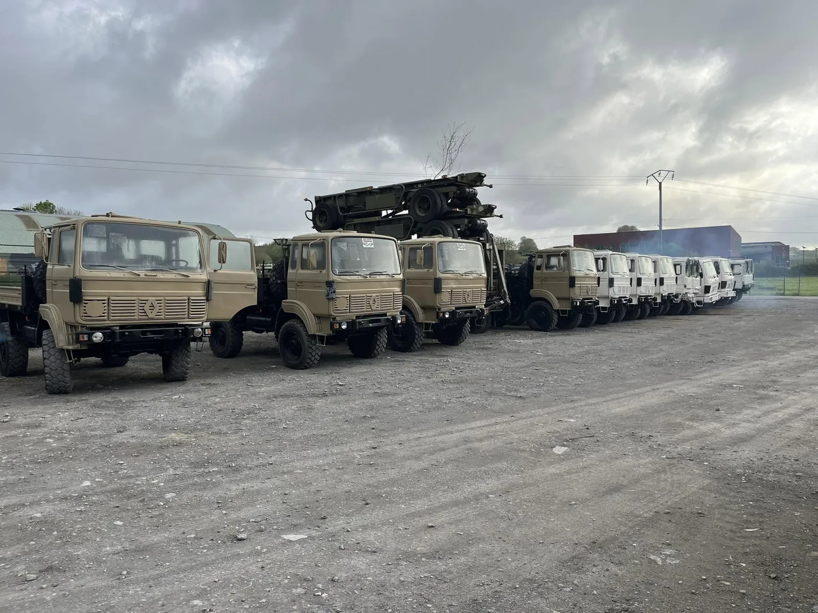 Camions Renault sable puis blancs alignés sur le parc sous un ciel gris