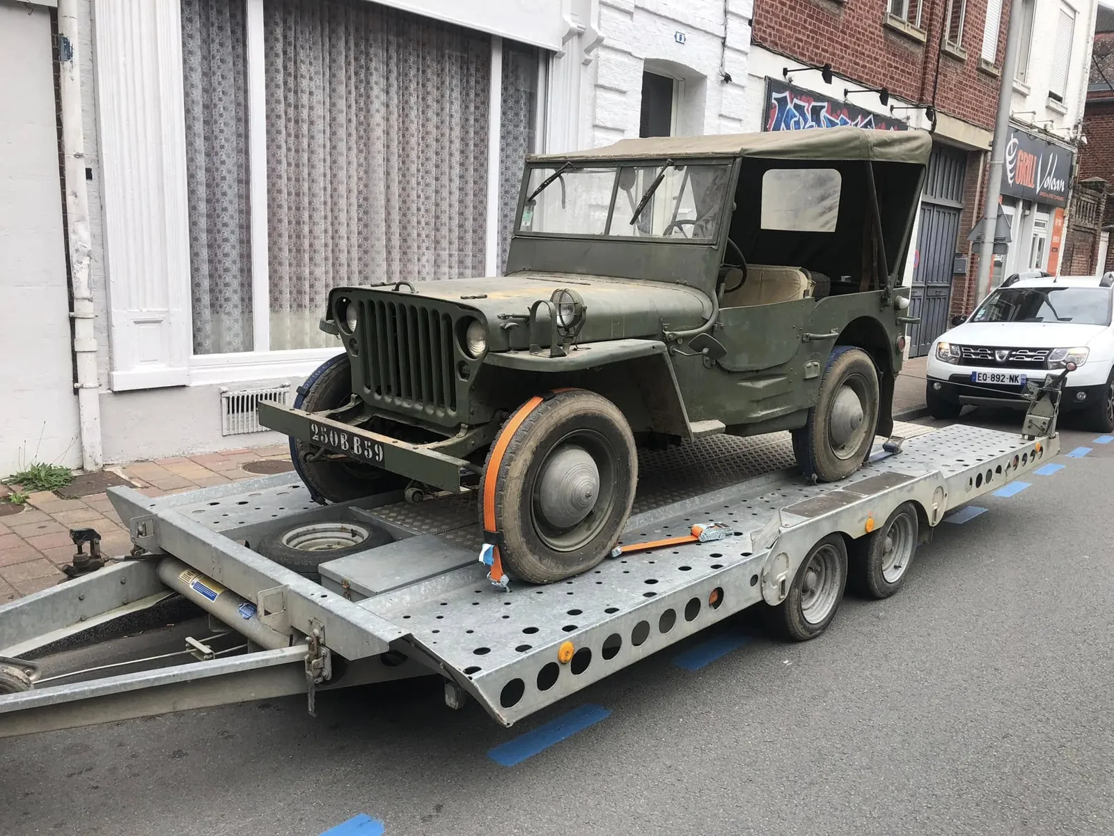Ford GPW sanglée sur un plateau porte-voiture dans une rue de Caudry, capote en place