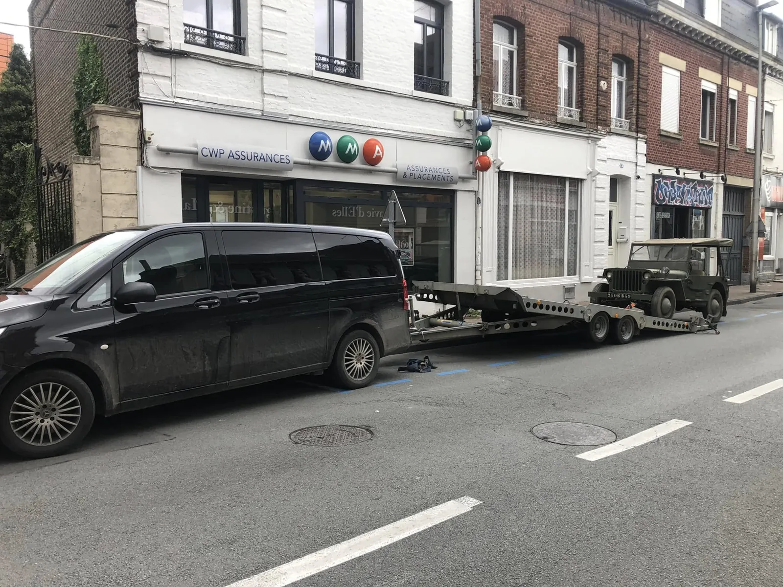 Fourgon et plateau portant la Ford GPW, stationnés devant des façades de Caudry