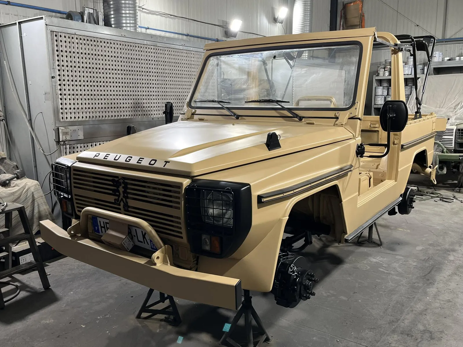 Peugeot P4 repeint en beige sable sur chandelles, roues déposées, dans la cabine de peinture
