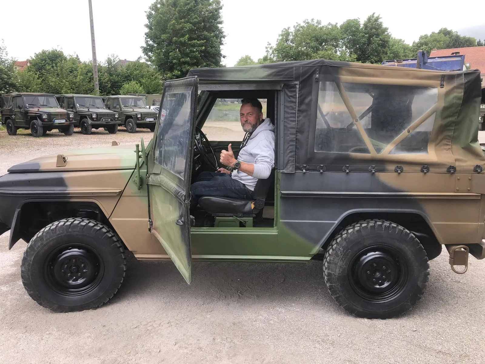 Client au volant d’un Peugeot P4 camouflage, porte ouverte, pouce levé avant le départ